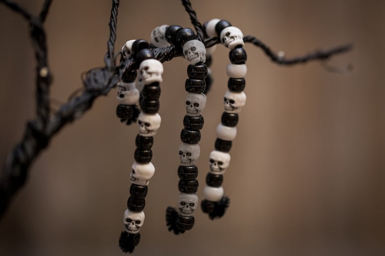 Op de afbeelding: Drie zwart-witte schedel kralen armbanden hangen aan een tak. De armbanden zijn gemaakt van afwisselende zwarte en witte kralen met schedel ontwerpen.