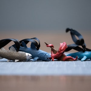 May include: Five colorful plastic sea creature ornaments with black ribbon hangers. The ornaments include a blue fish, a gray fish, a red octopus, and a blue sea serpent.
