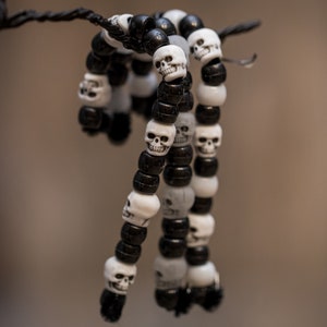 Op de afbeelding: Een zwart-wit kralenarmband met schedelbedels. De armband hangt aan een zwart koord.