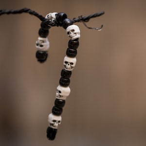 Op de afbeelding: Een zwart-witte schedel kralen armband die aan een tak hangt. De armband is gemaakt van zwarte kralen met witte schedel kralen.