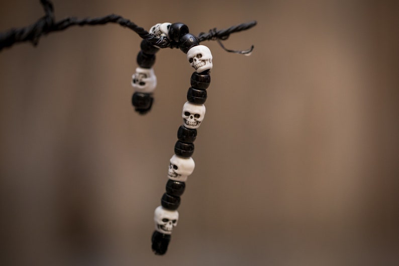 Op de afbeelding: Een zwart-witte schedel kralen armband die aan een tak hangt. De armband is gemaakt van zwarte kralen met witte schedel kralen.