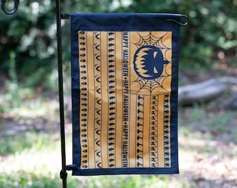 May include: A yellow and black Halloween garden flag with a black jack-o'-lantern face and the text "Happy Halloween" repeated four times.