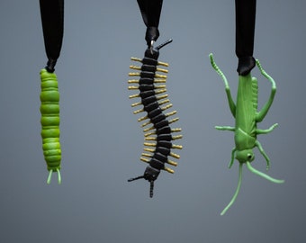 May include: Three hanging ornaments shaped like insects. A green caterpillar, a black and gold centipede, and a green grasshopper.
