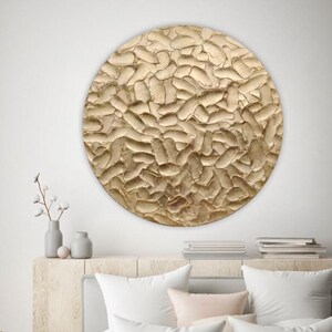 A high-end organic modern 3D textured round canvas in champagne gold. Displayed as a large statement piece above a neutral sofa in a quiet luxury chic apartment living room.