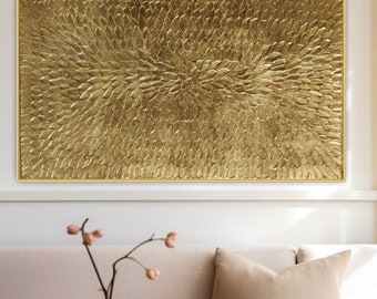 Puede incluir: Una gran obra de arte mural rectangular dorada texturizada con un marco dorado. La obra de arte tiene un patrón orgánico en relieve que irradia desde el centro. La pieza se exhibe sobre un sofá beige con un cojín decorativo.