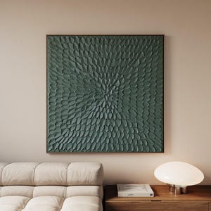 Könnte beinhalten: Ein quadratisches, gerahmtes Wandkunstwerk mit einer strukturierten, teal-grünen Oberfläche. Das Kunstwerk zeigt ein sich wiederholendes Muster, das von der Mitte ausgeht und ein dynamisches, organisches Design erzeugt. Der Rahmen ist dunkel und neutral.
