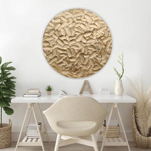 A round, textured wall art piece in shades of gold hangs above a white desk. The artwork has a raised, organic pattern. A white desk, chair, and decorative items complete the modern, neutral-toned office space.