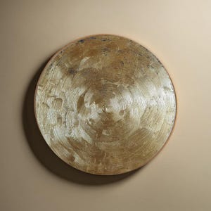 Op de afbeelding: Een rond, goudkleurig wanddecor met een getextureerd oppervlak. Het stuk heeft een ronde vorm en een metallic afwerking.