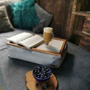 Puede incluir: Una bandeja rayada gris y blanca con un libro, un vaso de café y un cuenco de arándanos sobre una superficie de madera.