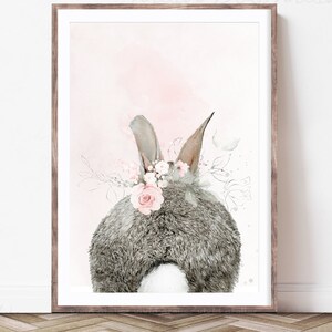 Puede incluir: Una pintura de acuarela de un conejo gris con una corona de flores rosas. El conejo est&aacute; de espaldas al espectador y el fondo es de color rosa suave.