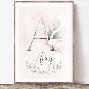 Puede incluir: Una impresi&oacute;n enmarcada con una ilustraci&oacute;n de acuarela de la letra A decorada con elementos florales rosas y verdes. El nombre "Amy" est&aacute; escrito en cursiva debajo de la letra.