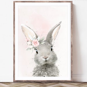 Puede incluir: Una pintura de acuarela de un conejo gris con flores rosas en su pelaje. El conejo est&aacute; mirando al espectador con grandes ojos marrones. El fondo es de un rosa suave.