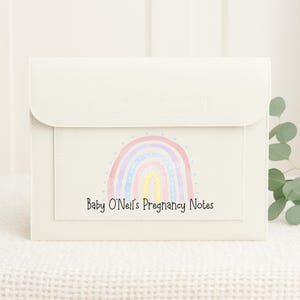 May include: A white folder with a rainbow design and the text "Baby O'Neil's Pregnancy Notes".