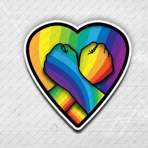 May include: A sticker featuring a heart shape with a black outline. Inside the heart are two fists, one purple and blue, the other yellow and orange, in a rainbow gradient. The sticker is on a white background.
