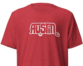 May include: Red t-shirt with the word "AUSTIN" in white, stylized text. The text is inside a white outline of a camper. The shirt is made of a soft, textured material.
