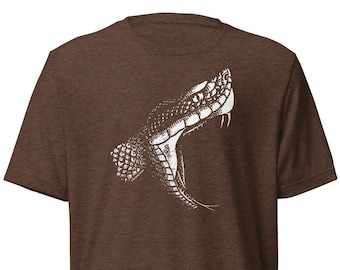 May include: Brown t-shirt featuring a detailed white illustration of a snake's open mouth, showcasing fangs and scales. The design is centered on the front of the shirt, creating a bold graphic statement. The shirt's fabric has a textured appearance.