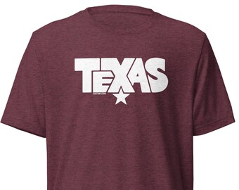 May include: Maroon t-shirt with the word "TEXAS" in large white block letters. A white star is centered below the text. The shirt also has the text "TEXAS FOR LIFE" in smaller white letters. The shirt is made of a soft material.