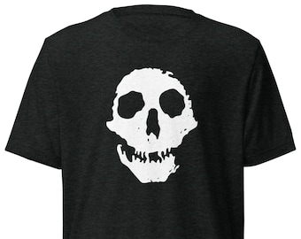 May include: Dark gray t-shirt featuring a white skull graphic on the back. The skull design is a simple, bold illustration with eye sockets, a nose cavity, and teeth. The shirt has a crew neck and short sleeves.