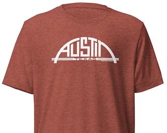 May include: A red heather t-shirt with a white graphic of the Austin, Texas skyline. The graphic features the words "Austin" and "Texas" in a stylized font.