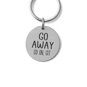 May include: A silver-colored keychain with a round pendant. The pendant has the words "GO AWAY" and "GO ON. GIT" in black, bold font. The keychain ring is also silver.