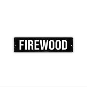 May include: A rectangular black metal sign with the word "FIREWOOD" in bold white capital letters. The sign has two small holes on each end for mounting. The background is plain white.