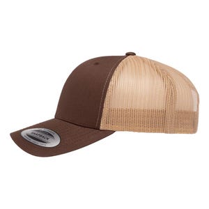 May include: A brown and tan trucker hat with a curved brim. The front panel is solid brown, while the back is tan mesh. A silver and black circular patch with the word "SNAPBACK" is on the front.
