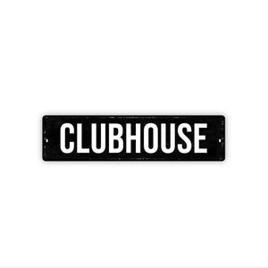 May include: A rectangular black metal sign with the word "CLUBHOUSE" in white, uppercase letters. The sign has a distressed appearance and is mounted on a white background. The sign has two small holes on each end.