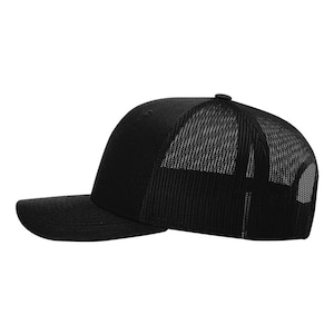 May include: A black trucker hat with a curved brim. The front panel is solid black, while the back features a black mesh for ventilation. The hat has a standard six-panel design and a snapback closure for an adjustable fit.
