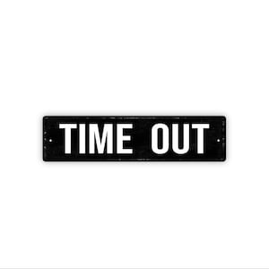 May include: A rectangular black sign with the words "TIME OUT" in bold white capital letters. The sign has a slightly distressed appearance, suggesting a vintage or rustic style. The background is plain white.