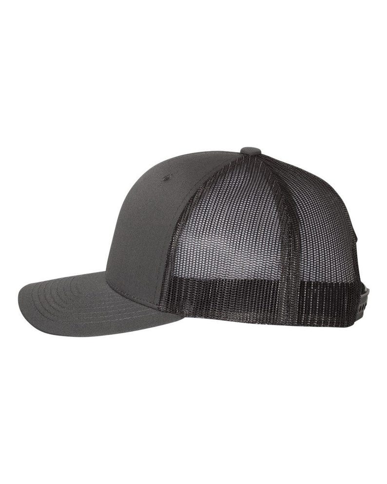 May include: A charcoal gray trucker hat with a curved brim and a mesh back. The hat features a solid front panel and a snapback closure for an adjustable fit. The mesh back provides ventilation.