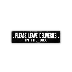 May include: Black rectangular sign with white text that reads "PLEASE LEAVE DELIVERIES - IN THE BOX -". The sign is centered on a white background. The text is in a bold, sans-serif font.