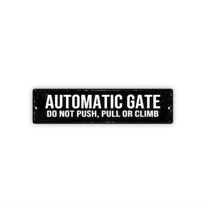 May include: A rectangular black metal sign with the words "AUTOMATIC GATE" in white capital letters. Below, the text reads "DO NOT PUSH, PULL OR CLIMB". The sign has two small holes for mounting.