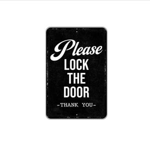 May include: A rectangular black metal sign with rounded corners and white text that reads Please LOCK THE DOOR -THANK YOU-. The sign features a distressed, textured finish with small mounting holes at the top and bottom center edges.