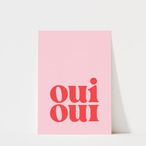 May include: A rectangular art print featuring a solid light pink background with the word "oui" printed twice in a stacked format using a bold, red, serif typeface. The text is centered in the lower half of the vertical print.