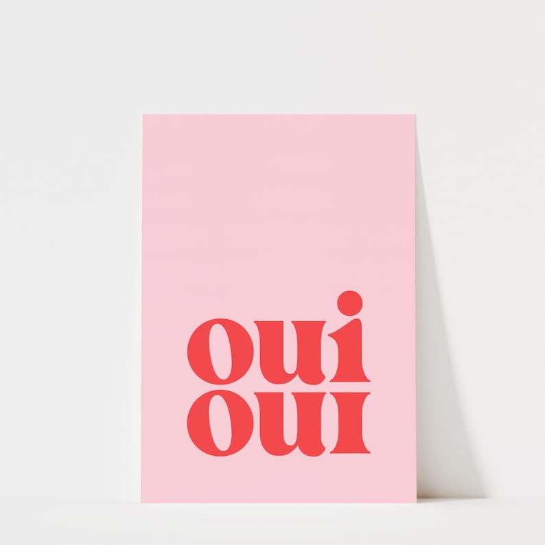 May include: A rectangular art print featuring a solid light pink background with the word "oui" printed twice in a stacked format using a bold, red, serif typeface. The text is centered in the lower half of the vertical print.