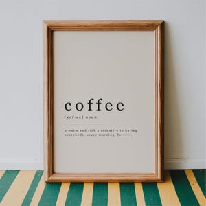 May include: A rectangular wall art print in a light wood frame featuring a dictionary-style definition of the word coffee. The text reads: coffee [kof-ee] noun, a warm and rich alternative to hating everybody, every morning, forever.