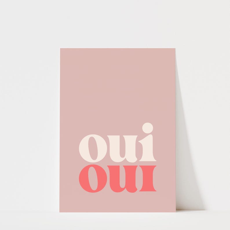 May include: A rectangular wall art print featuring a dusty rose background. The word "oui" is printed twice in a stacked, bold, serif typeface. The top "oui" is in a creamy off-white color, while the bottom "oui" is in a vibrant coral pink.