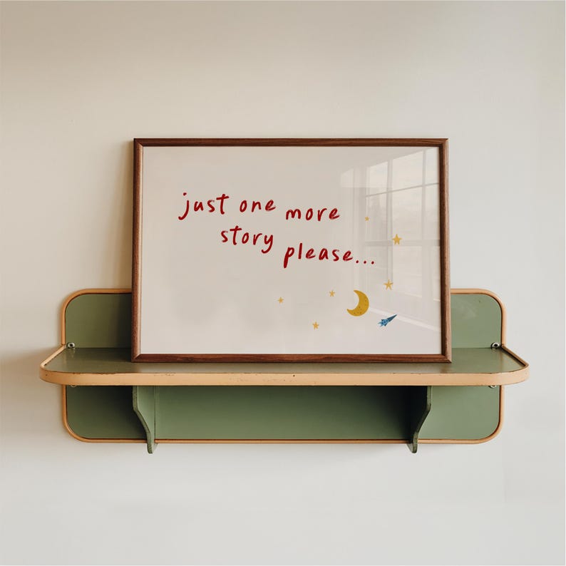 A framed whiteboard with the text "just one more story please..." written on it, placed on a green shelf against a white wall.