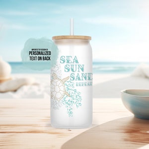 May include: White tumbler with a sea turtle, seaweed, and the text "Sea Sun Sand Repeat" in teal blue. The tumbler has a wooden lid and a straw.