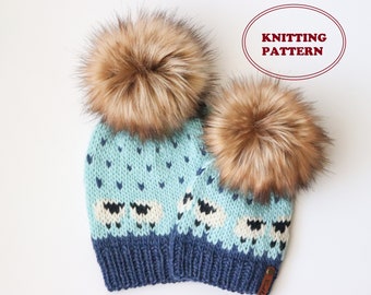 Könnte beinhalten: Zwei gestrickte Mützen mit blauen und weißen Schafmotiven und Kunstfellbommeln. Die Mützen sind blau und hellblau mit weißen Schafen und Herzen. Die Bommeln sind braun. Die Mützen sind mit "Strickmuster" beschriftet.