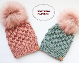 May include: Two knitted hats with faux fur pom poms. The hats are in a textured stitch and are in shades of dusty rose and teal.