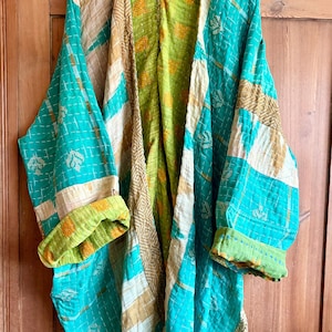 May include: A long-sleeved open-front jacket featuring a patchwork design with vibrant turquoise, lime green, and tan fabric panels. The garment is detailed with intricate white running stitch embroidery throughout and has folded cuffs.