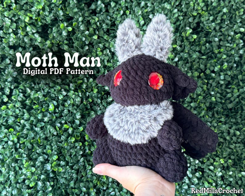 May include: Black crocheted moth plush toy with red eyes and gray fur accents. The toy is being held by a hand. The text "Moth Man Digital PDF Pattern" is visible in the image.