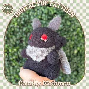 May include: A plush toy in the shape of a mothman, with a black and grey fuzzy body, red eyes, and grey wings. The toy is being held in a hand against a green leafy background. The text "Chubby Mothman" is printed below the toy.