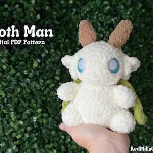 May include: A white crocheted moth creature with brown and green wings. The creature has large blue eyes and a fluffy texture. The text "Moth Man Digital PDF Pattern" is visible in the image.