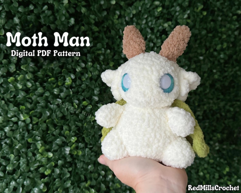 May include: A white crocheted moth creature with brown and green wings. The creature has large blue eyes and a fluffy texture. The text "Moth Man Digital PDF Pattern" is visible in the image.