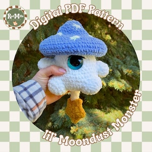 Könnte beinhalten: Handgehäkeltes "lil' Moondust Monster" Plüschtier. Das skurrile Wesen hat eine blaue Pilzkappe mit weißen Sternen, große blaue Augen und einen flauschigen weißen Körper. Der Text "Digital PDF Pattern" und "Red Mills Crochet" sind sichtbar.