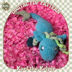 May include: A crocheted blue and green Kelpie named Karl, lying on a bed of pink flower petals. The crocheted Kelpie has a long tail and a mane of green yarn. The text "Karl the Kelpie" is written below the Kelpie.