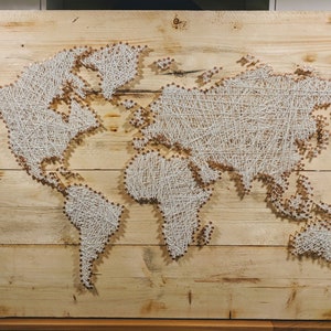 May include: A world map created with string art on a wooden board. The map is made with white string wrapped around nails hammered into the wood. The continents are outlined in white string.
