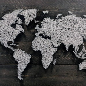 May include: A white string art world map on a dark wood background. The map is made of white string wrapped around nails hammered into the wood.